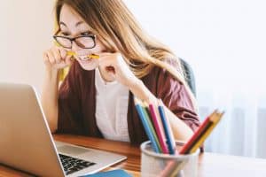Femme manager stressée mordant un stylo devant son ordinateur, illustrant la charge mentale des femmes au travail.